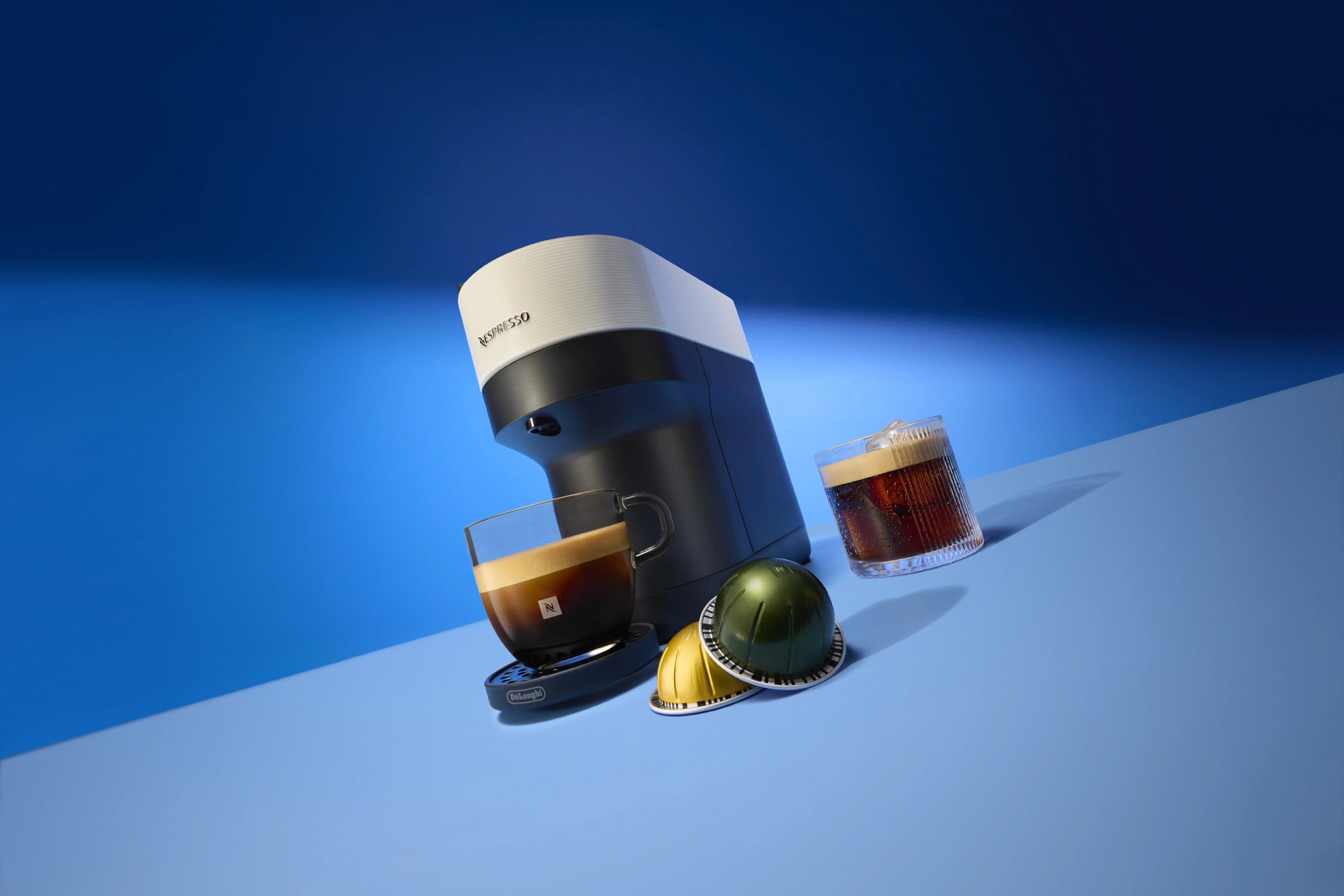 Nespresso Ispirazione Italiana: koffiemachine, kopjes en capsules op een blauwe achtergrond