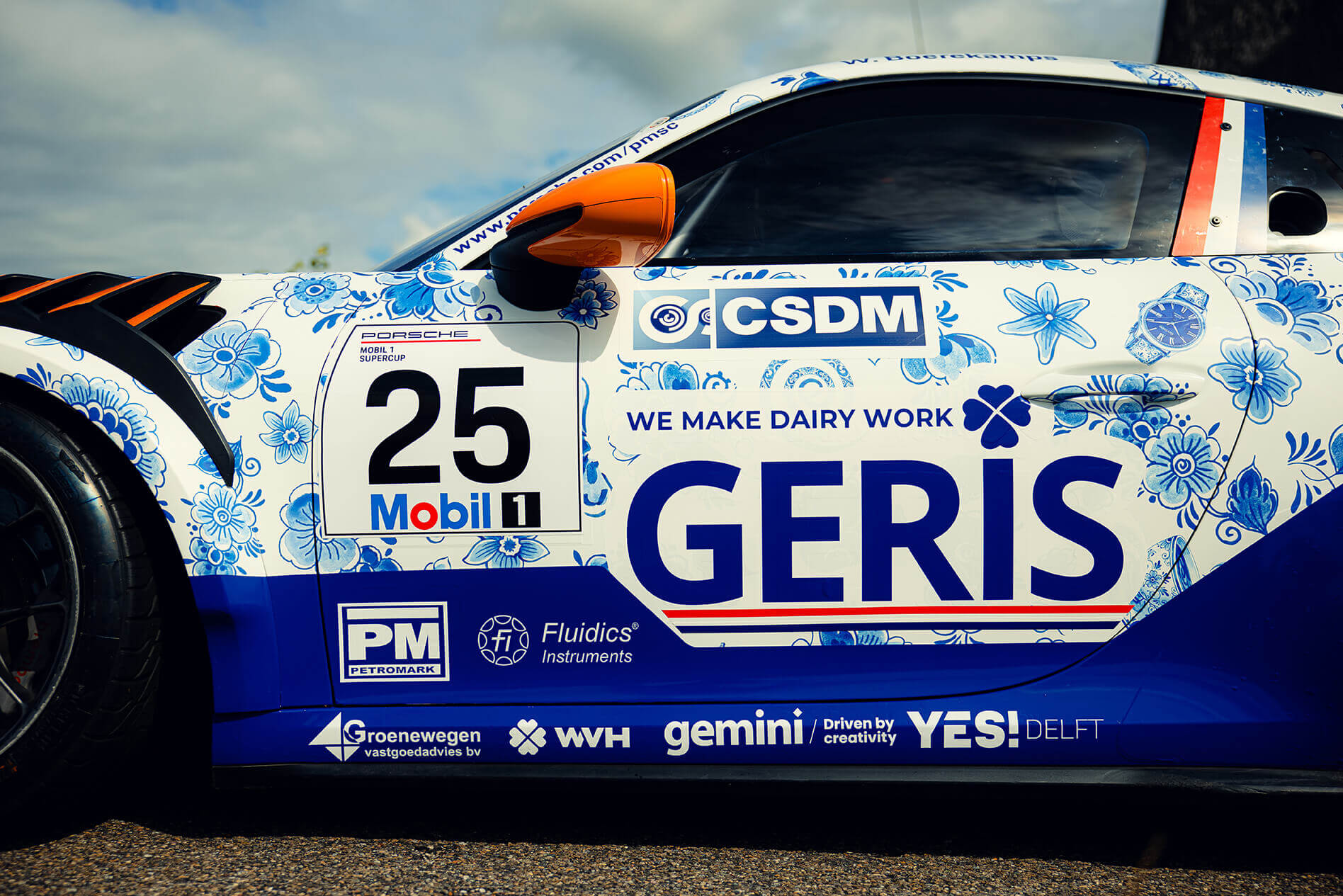 Race car side with blue floral wrap, orange side mirror, number 25, and sponsor logos along the door silled with 'GERIS' seen in large letters